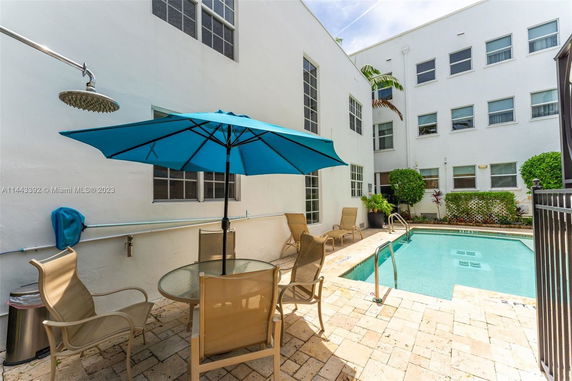 Outdoor area with a swimming pool, chairs, and an umbrella beside a multi-story building.
