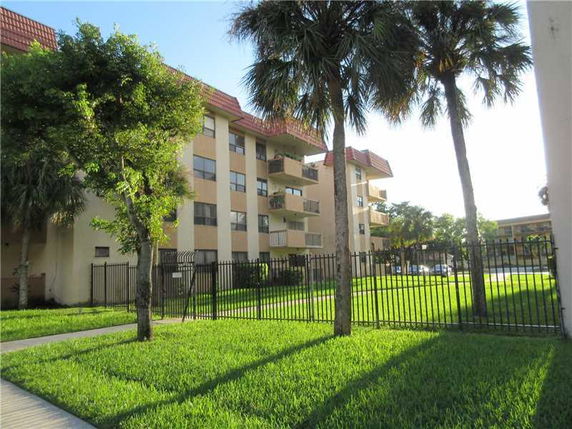 Front view of a multi-story apartment building with balconies and a fenced lawn area.