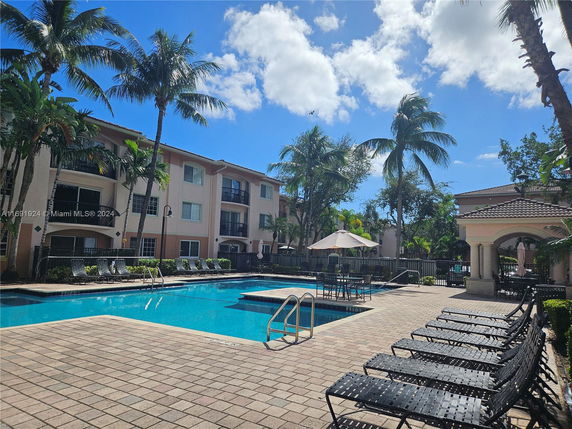 Outdoor swimming pool area surrounded by apartment buildings and palm trees.