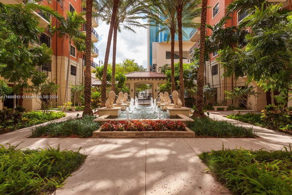 View of a courtyard with a central fountain and surrounding greenery and buildings.