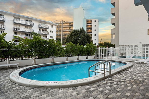 Outdoor area with a swimming pool surrounded by buildings and plants.