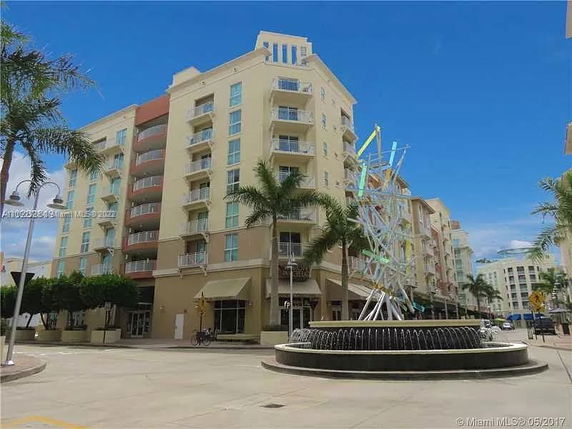Front view of a multi-story apartment building with balconies and a decorative fountain.