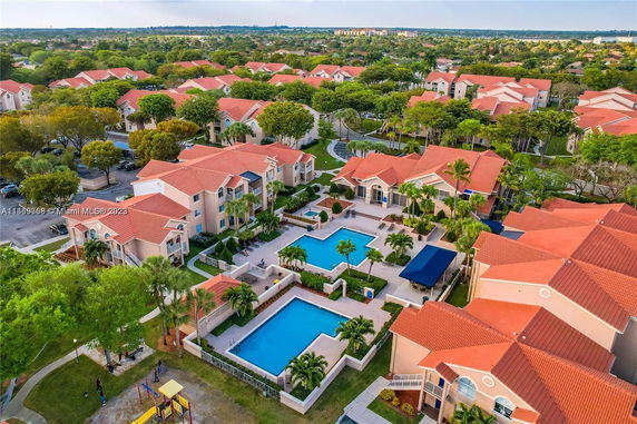 Aerial view of a residential complex with multiple buildings and swimming pools amidst green surroundings.