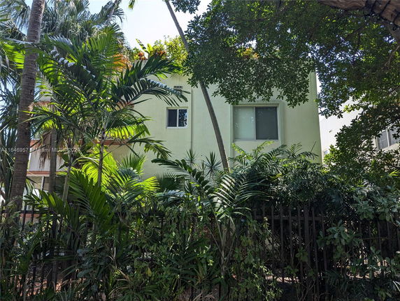 Front view of a two-story house with windows partially obscured by trees and plants.