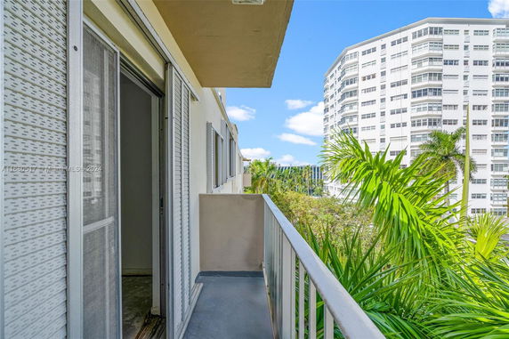 View from a balcony showing a tall residential building and palm trees nearby.