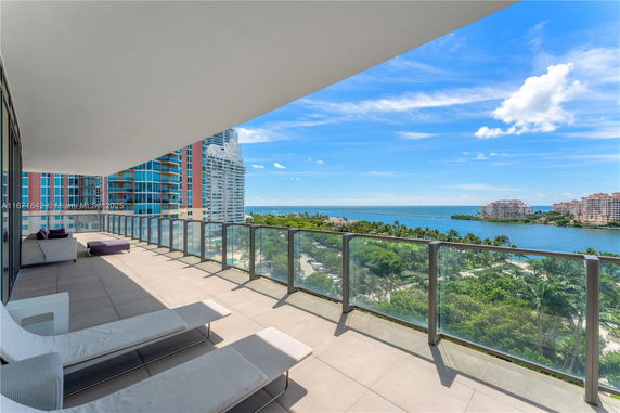Spacious balcony with glass railing offering a panoramic view of buildings and water.