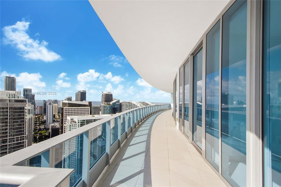 Panoramic view from a high-rise building balcony with glass railings, overlooking city skyscrapers.