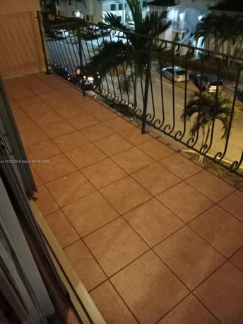 View from a balcony overlooking a street with parked cars and palm trees.