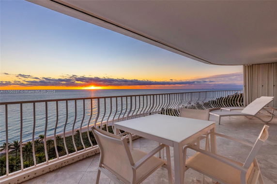 Panoramic view of the ocean from a balcony with chairs and a table.
