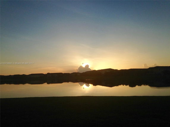Panoramic view of a lake reflecting the sunset with silhouettes of houses in the background.