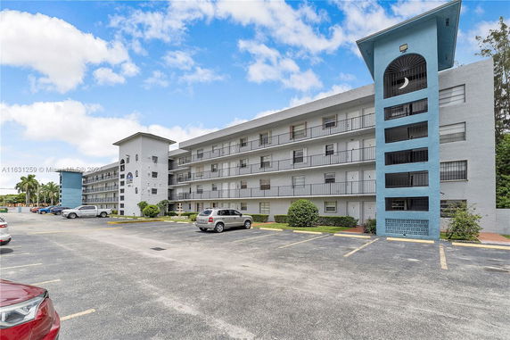 Front view of a mid-rise apartment building with balconies and parking area.