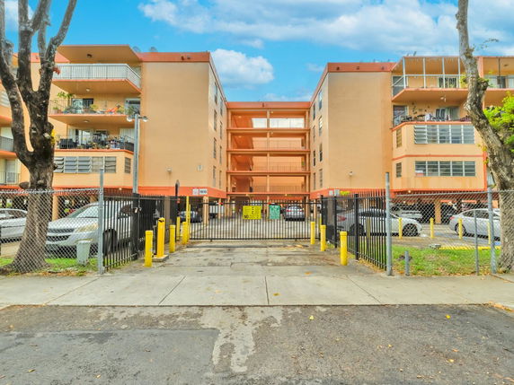 Front view of a multi-story apartment building with a gated entrance and parking area.