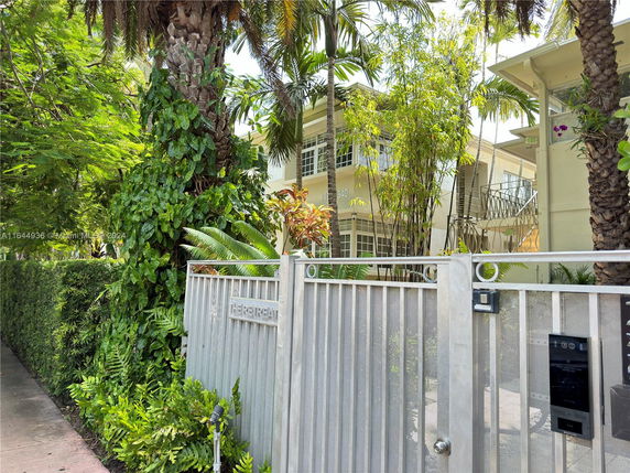 Front view of a house with a gated entrance surrounded by lush greenery.