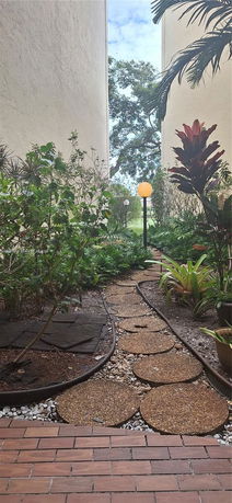 Outdoor garden pathway between two buildings with plants and trees.