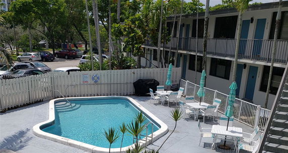 Outdoor area with a swimming pool surrounded by a fence and seating with umbrellas.