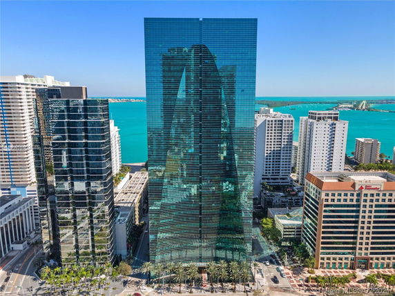 View of tall glass-covered skyscraper surrounded by other high-rise buildings near a body of water.