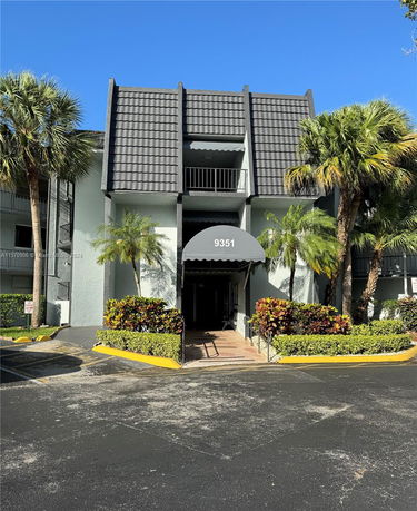 Front view of a three-story building with an awning labeled 9351 and decorative plants.