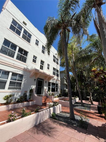 Front view of a multi-story residential building with large windows and surrounding palm trees.