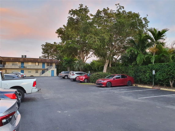 Outdoor parking area with multiple parked cars and trees in the background.