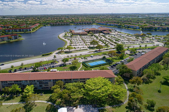 Panoramic view of a residential area with buildings, a lake, parking lots, and tennis courts.