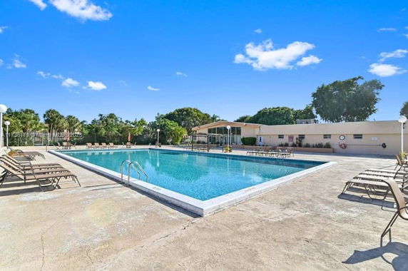 Outdoor swimming pool area with lounge chairs and surrounding trees.