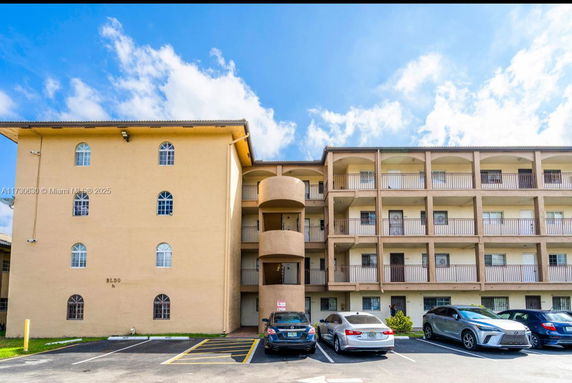 Front view of a multi-story residential building with balconies and parking area.