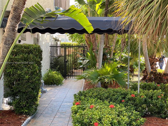 Pathway leading to a gated entrance with surrounding greenery and a canopy.