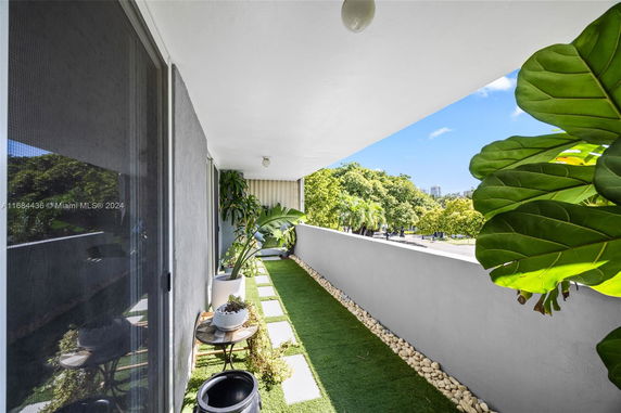 Balcony with artificial grass and plants offering a view of the surrounding trees and cityscape.