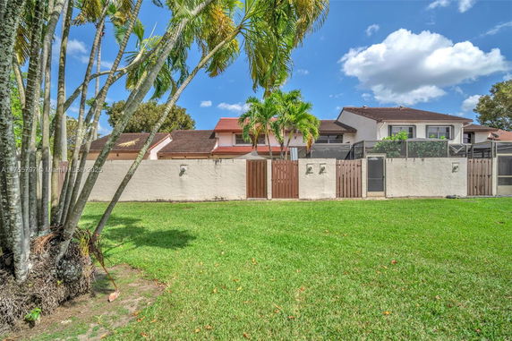 Front view of a two-story house with red roof, surrounded by a fence and palm trees.
