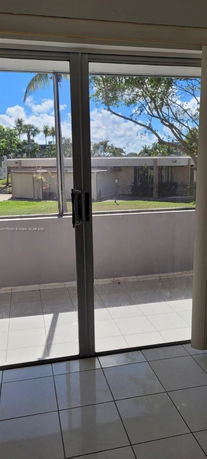 View through a glass door showing the exterior surroundings with trees and nearby building.