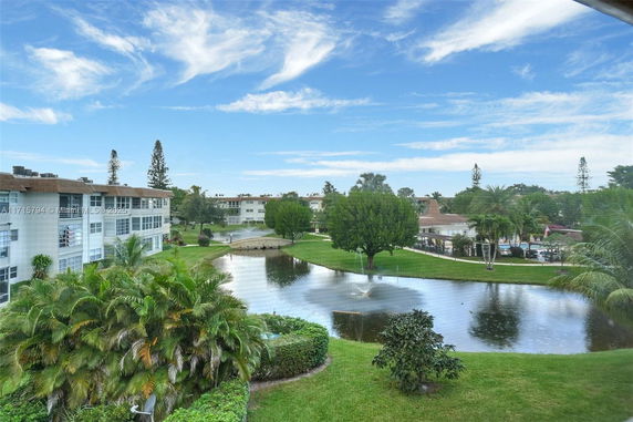 Outdoor view of apartment buildings with a pond and landscaped trees.