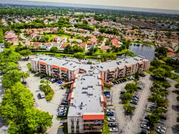Aerial view of an apartment complex with multiple buildings and parking areas, surrounded by greenery and other residential structures.