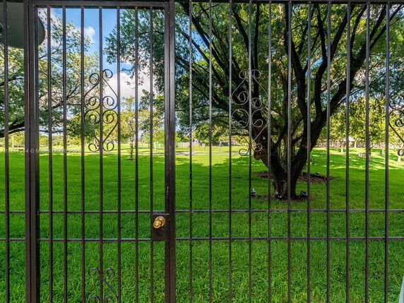 View from behind a black metal gate overlooking a grassy park area with trees.