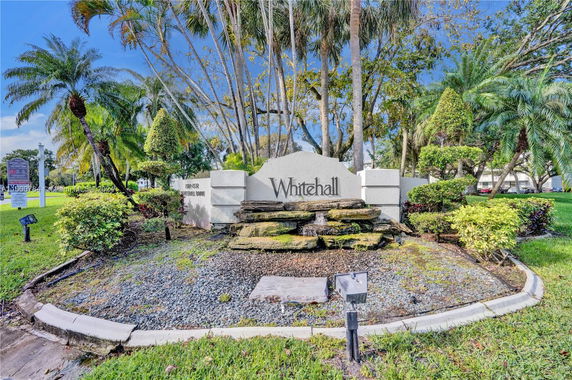 Entrance sign for the Whitehall community with landscaping and palm trees.