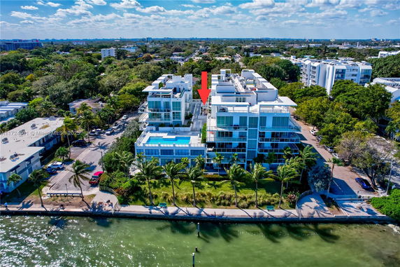 Aerial view of a waterfront apartment complex with modern design and a nearby parking area.