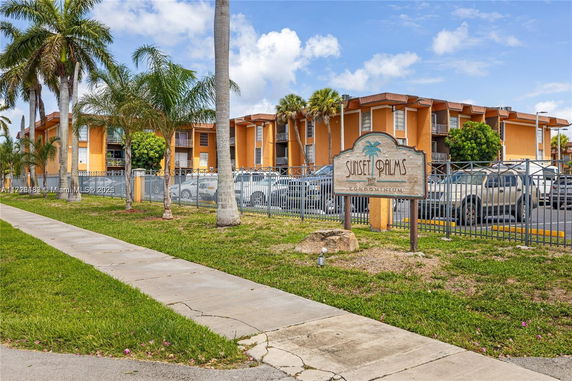 Front view of a condominium building with an orange facade and fenced parking area.