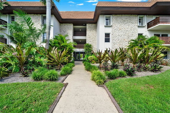 Front view of a multi-story building with stone and white exterior, surrounded by lush landscaping.