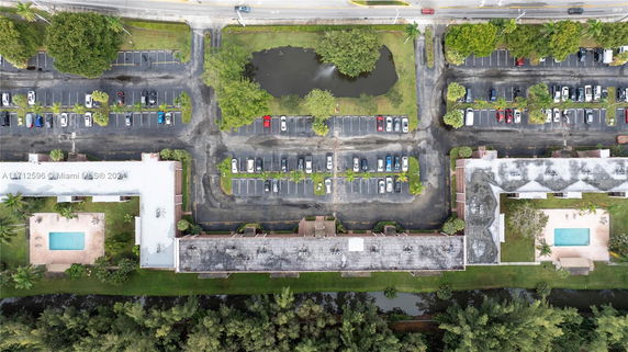 Aerial view of a parking lot with multiple cars next to buildings and a small pond.