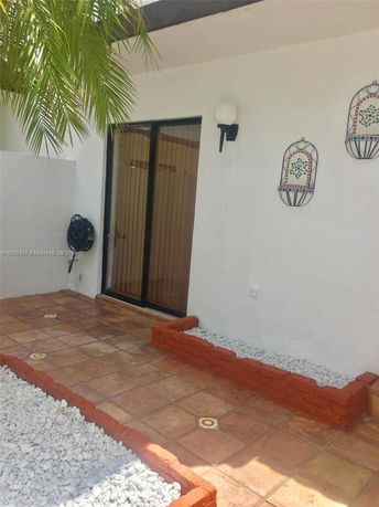Front view of a building with a tiled patio and sliding glass door.