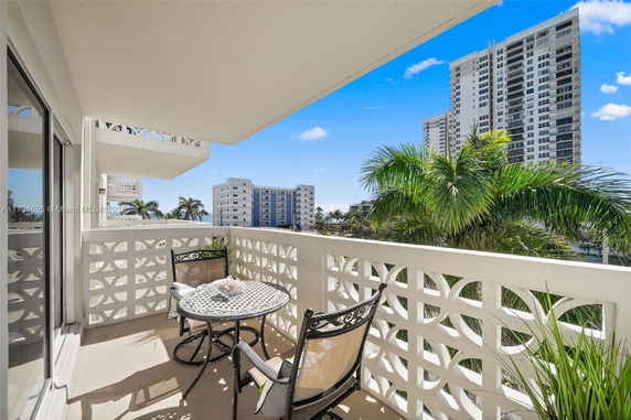 Balcony with outdoor seating overlooking palm trees and high-rise buildings