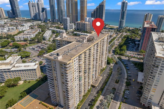 Aerial view of a tall apartment building with visible rooftop features and surrounding cityscape leading to the ocean.