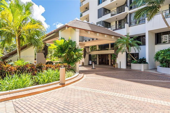 Front view of a modern multi-story building with a covered entrance and tropical landscaping.