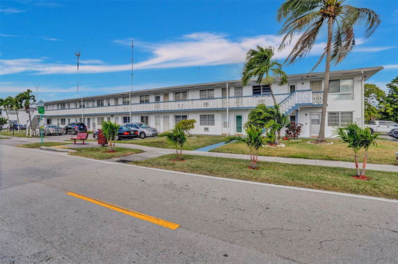 Front view of a two-story residential building with parking spaces and palm trees.