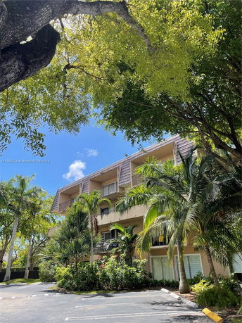 Front view of a multi-story residential building with balconies and surrounding greenery.