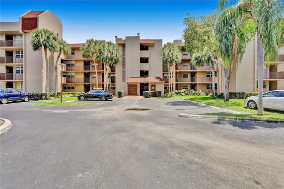 Front view of a multi-story apartment building with balconies and palm trees.