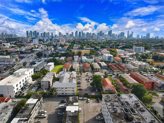 Aerial view showing a mix of low-rise buildings and high-rise city skyline in the background under a clear blue sky.