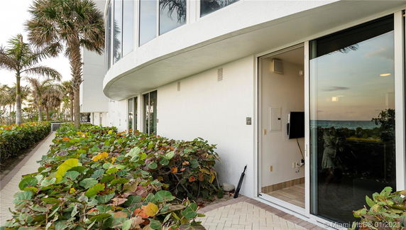 Exterior view of a building with a path surrounded by greenery and large windows reflecting the ocean.