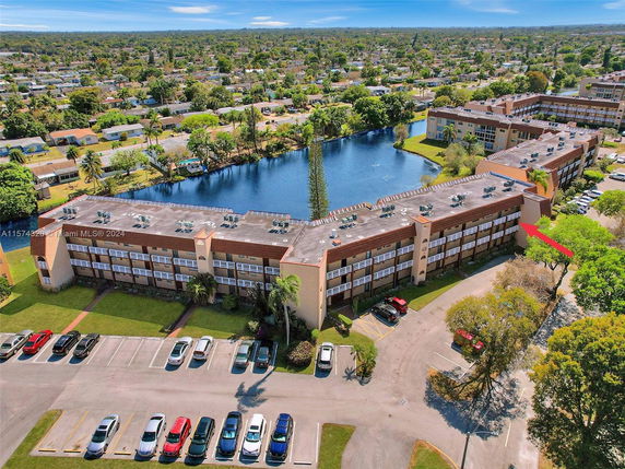 Aerial view of an apartment complex near a water body surrounded by residential houses and trees.
