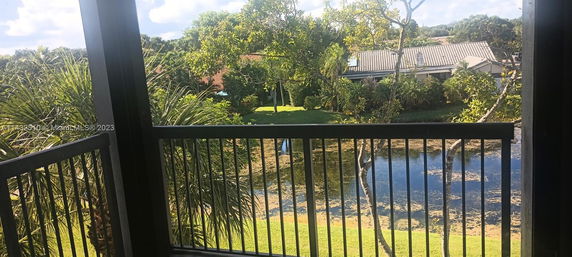 View from a balcony overlooking greenery, a pond, and houses in the distance.