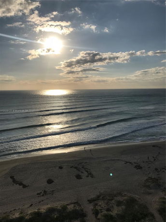 Panoramic view of a beach with the sun setting over the ocean.